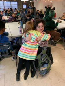 Rosabella hugging a student in the dining hall, their face unseen.